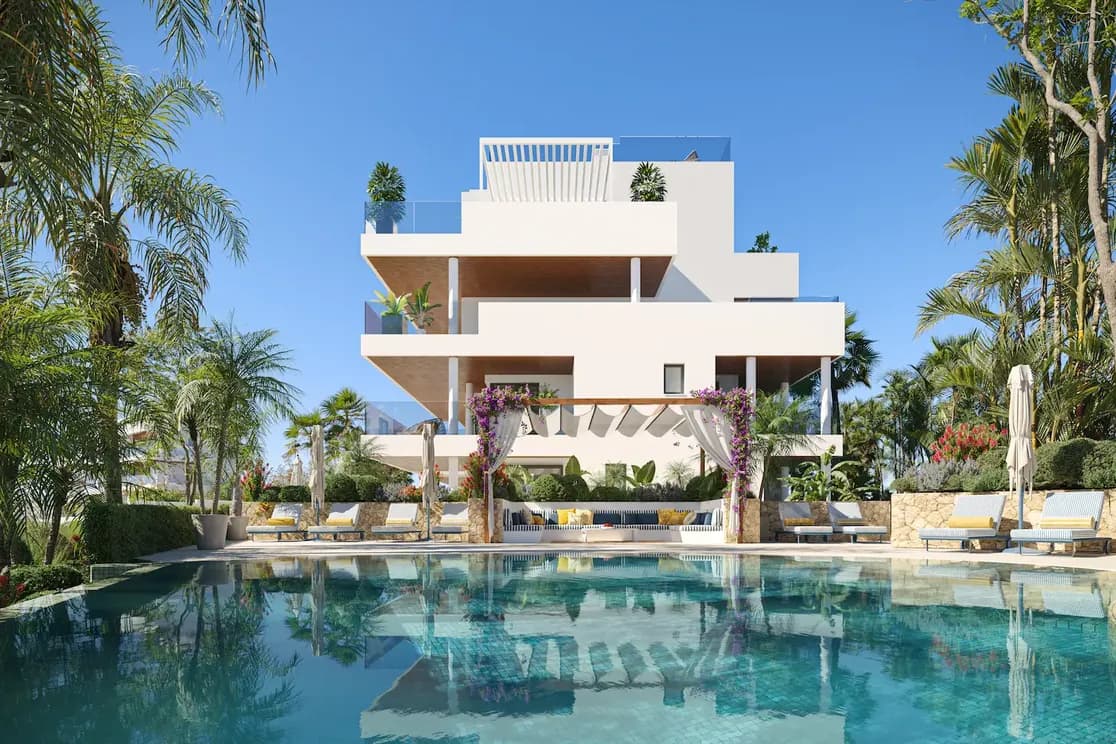 Gemeinschaftsschwimmbad in einer Luxusanlage in Marbella mit einem Apartmentgebäude im Hintergrund, umgeben von grüner Vegetation und klarem blauen Himmel