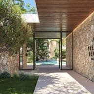 Luxury entrance of Precious Benalus with tree on the left and stone wall on the right, in the background you can see a swimming pool