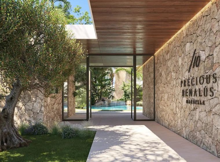 Luxuriöser Eingang von Precious Benalús mit einem Baum auf der linken Seite und einer Steinmauer auf der rechten Seite, im Hintergrund ist ein Schwimmbad zu sehen