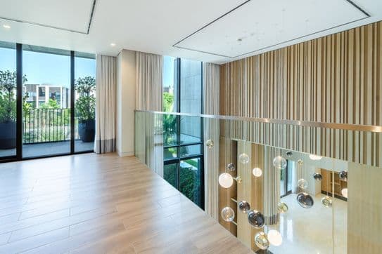 Modernes Interieur mit Holzboden, Glasgeländer und hängenden kugelförmigen Leuchten. Große Fenster bieten einen Blick auf das Grün im Außenbereich.