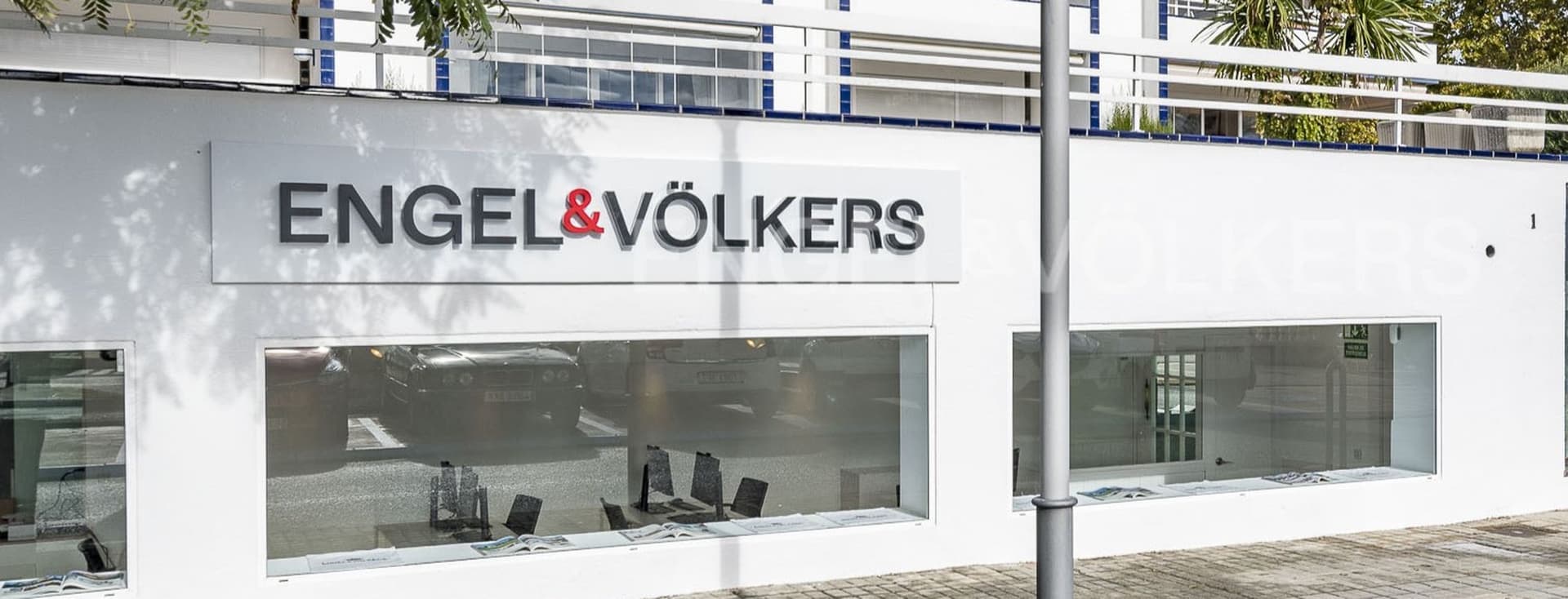 Oficina immobiliària Engel & Völkers amb una façana blanca i grans finestrals que mostren propietats.