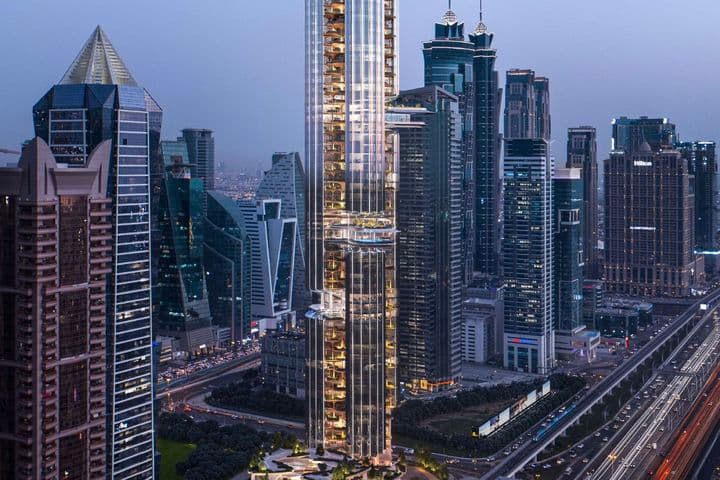 A tall, modern skyscraper in an urban skyline at dusk, surrounded by other high-rise buildings and busy highways with streaking car lights.