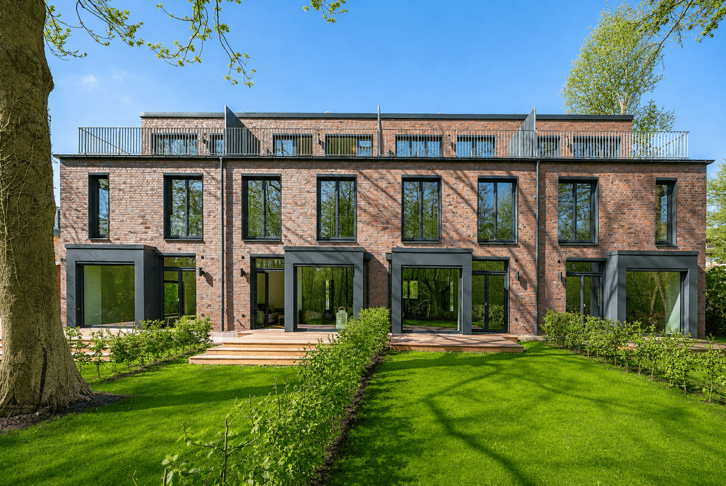Modern three-story brick building with large black-framed windows, ground-level patios, manicured green lawn and trees under a clear blue sky.