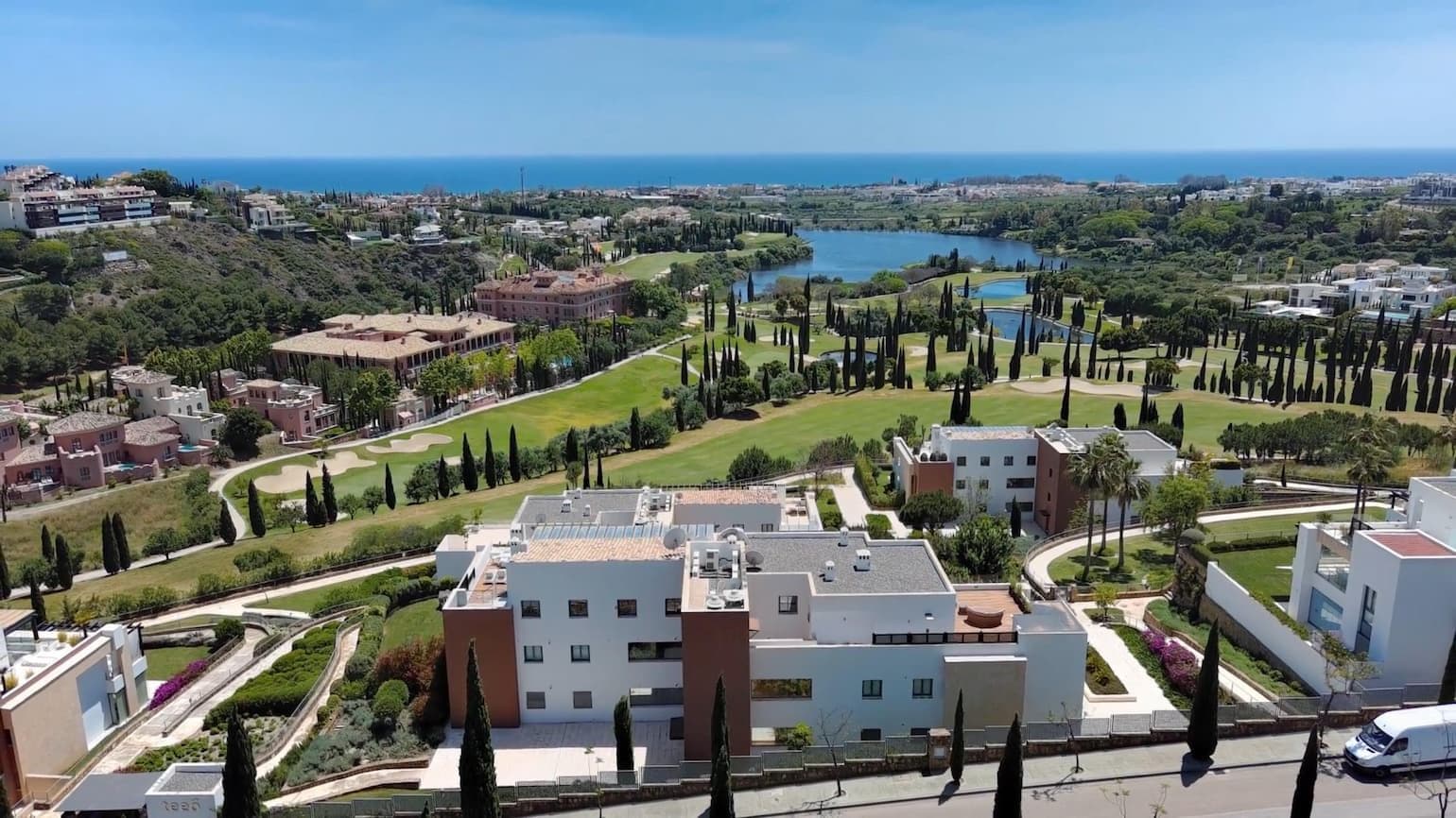 Vista del camp de golf de Los Flamingos amb un edifici blanc al fons i vistes al mar al final.