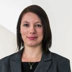 A professional woman in formal attire, standing confidently against a neutral background with a subtle smile.