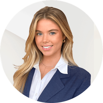 Smiling person with long blonde hair wearing a blue blazer and white shirt against a light background.