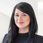 Portrét Ilony Fanfrdlové. Žena s rovnými tmavými vlasy, v černém saku a černém topu, pózuje před světlým pozadím s jemným úsměvem.