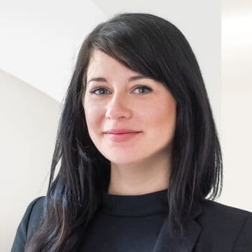 Portrait of Ilona Fanfrdlová. A woman with straight dark hair, wearing a black blazer and black top, posing in front of a light background with a soft smile.