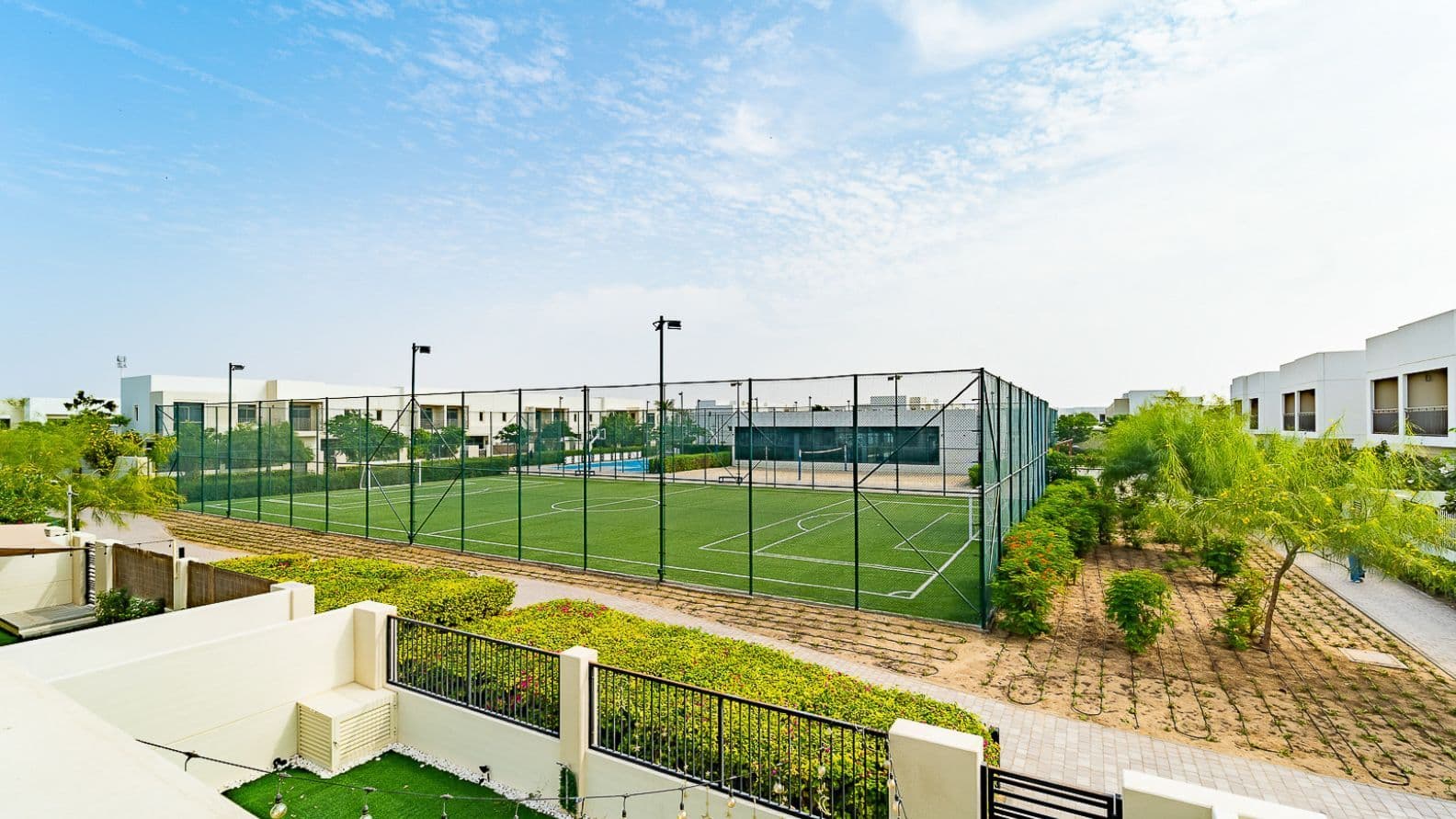 Green fenced football pitch in the heart of a Town Square Dubai villa community, surrounded by landscaped gardens and low-rise homes.