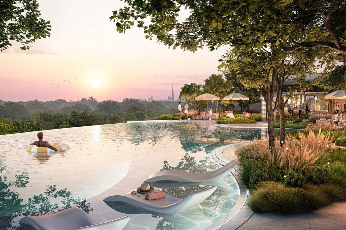 Ein Mann treibt bei Sonnenuntergang in einem Gummiring im Pool, während andere sich entspannen und unterhalten – mit Ausblick auf Distrikt und die Skyline von Downtown Dubai.