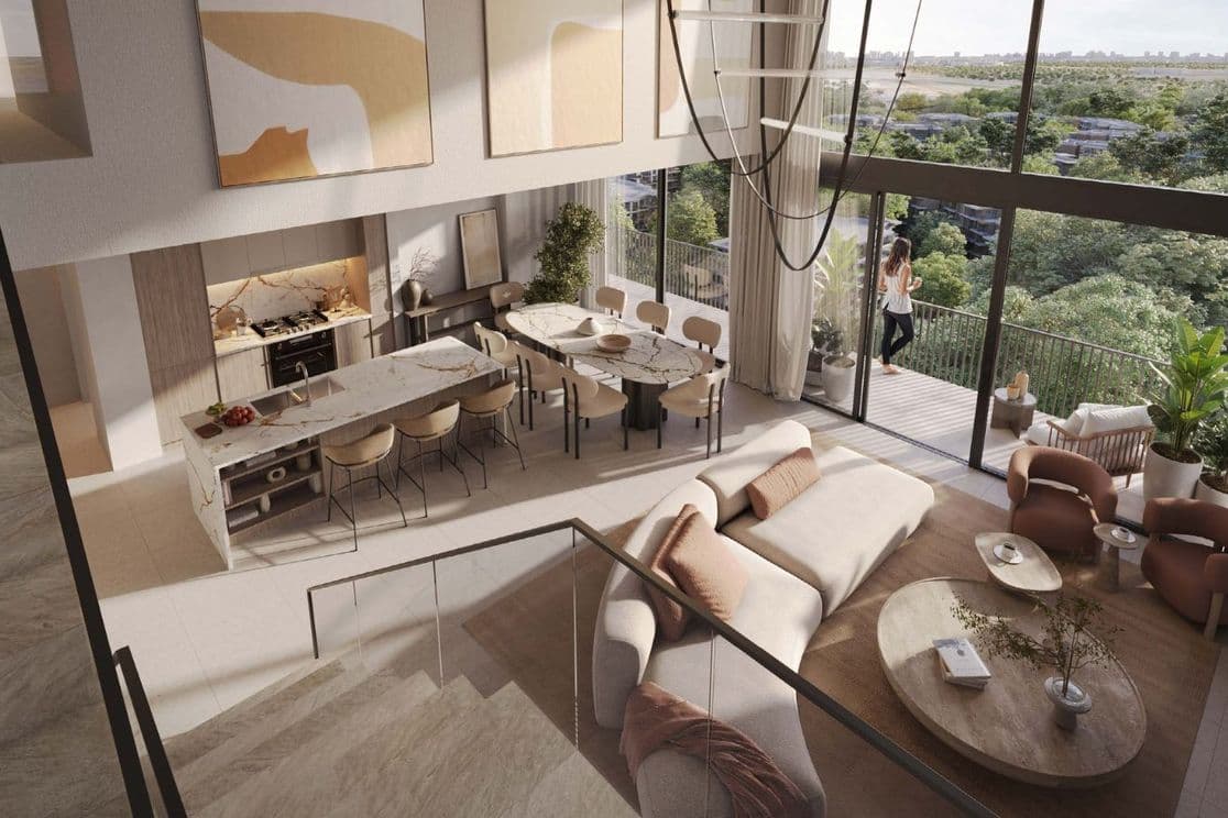 Frau steht auf dem Balkon eines Maisonette-Apartments in Distrikt und blickt auf das Grün der Ghaf Woods Community.