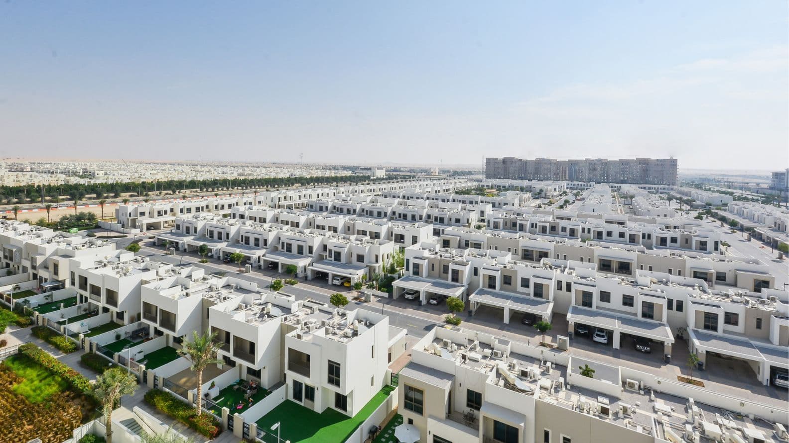 Weitwinkel-Luftaufnahme der ordentlich angeordneten weißen Stadthäuser in Town Square Dubai, mit großzügigem, einheitlichem Grundriss und baumgesäumten Straßen.
