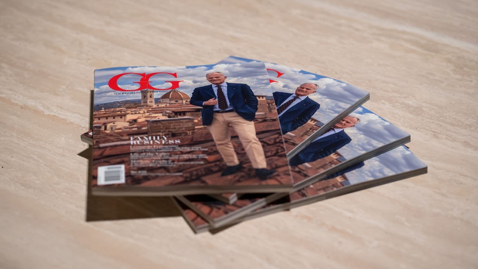 Stack of GG magazines on a table, featuring a cover image of a person in a suit standing outdoors with a cityscape background.