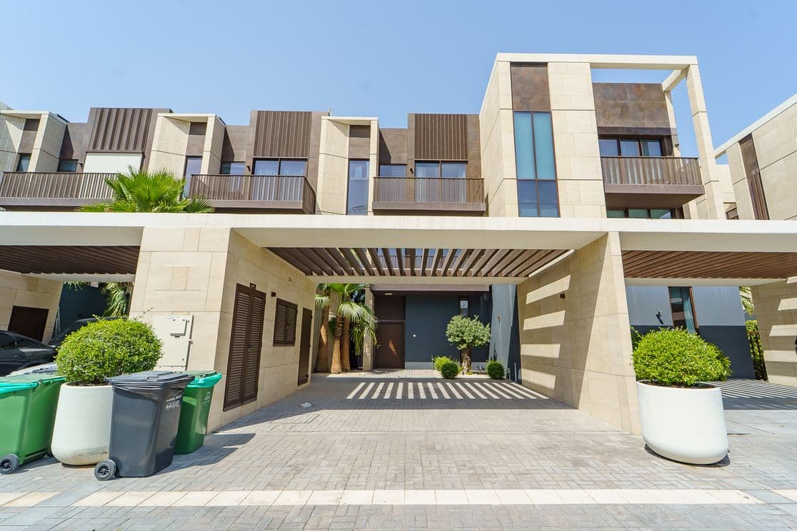 Modernes Stadthaus mit großen Fenstern, Holzakzenten und einem Carport. Begrünung in Pflanzgefäßen und Recyclingbehälter sind in der Einfahrt sichtbar.