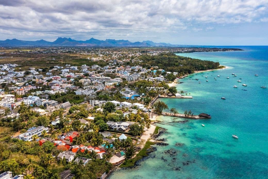 Aerial view of Mont Choisy with turquoise waters, boats, sandy beaches, lush greenery, and distant mountains under a partly cloudy sky.