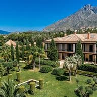 Luxury villa in Nagüeles surrounded by green fauna, in front of Marbella's La Concha mountain and a clear blue sky.