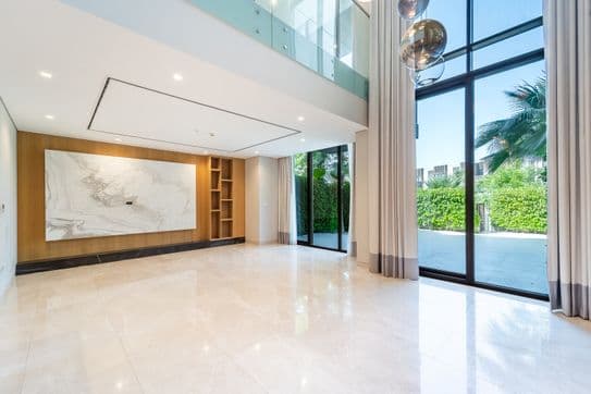 Geräumiges, modernes Wohnzimmer mit Marmorböden, großformatiger abstrakter Wandkunst, bodentiefen Fenstern und Blick auf das Grün im Außenbereich.