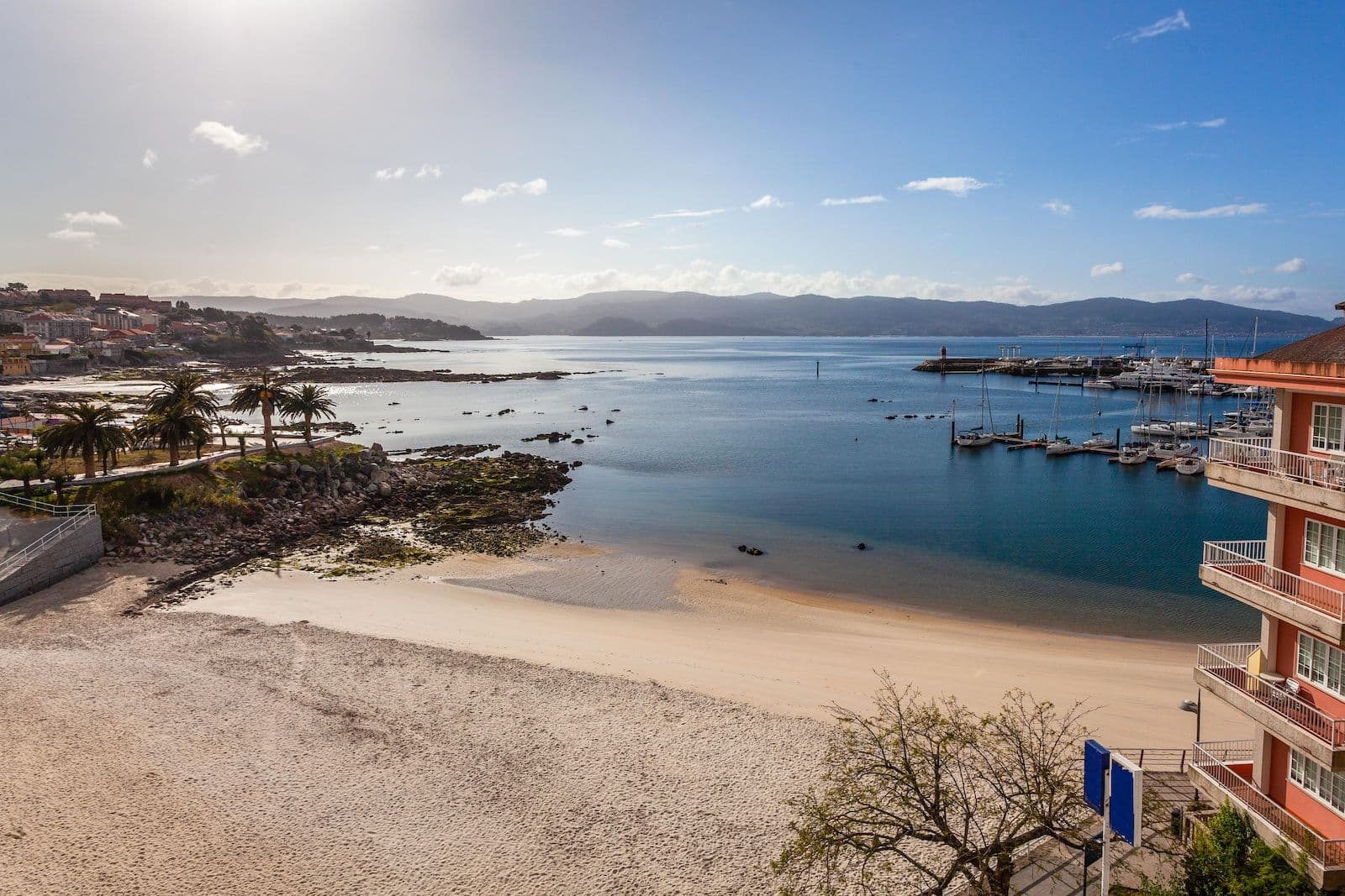 Vista de la platja de Panadeira amb edificis a la dreta, palmeres a l'esquerra i el port a l'horitzó.