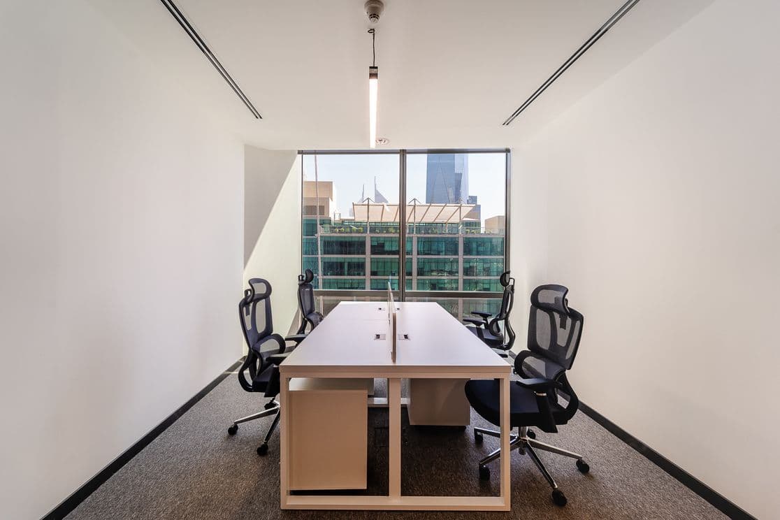 Modern office space with two workstations, ergonomic chairs, and a large window overlooking urban buildings. Bright and minimalist design.