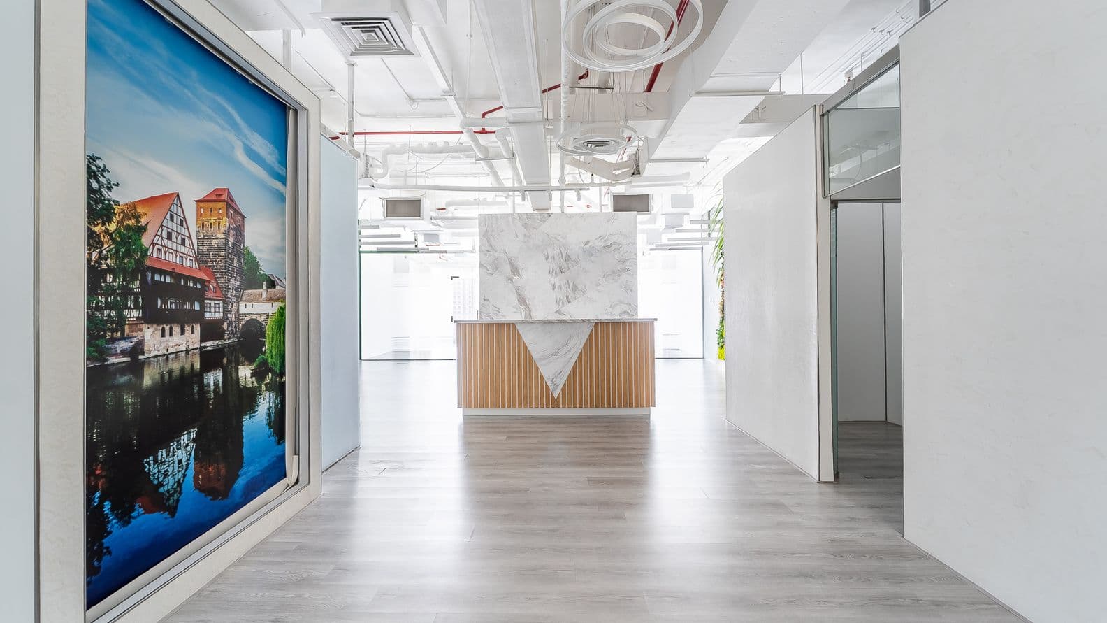 Bright modern office lobby with marble-topped reception desk, wood-slat base, open white ceiling and waterfront mural on the left.