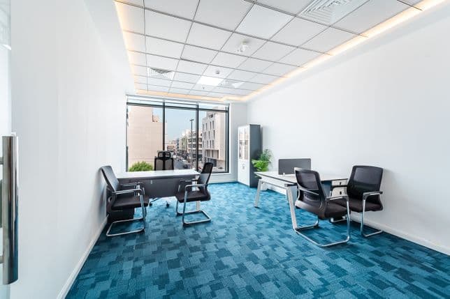 Private office space inside Burj Nahar Building with internal glass wall, two desks, black chairs, storage cabinet, and accent lighting.
