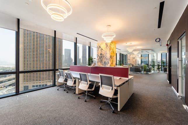 Modern office interior in Boulevard Plaza with workstations, floor-to-ceiling windows overlooking Dubai skyscrapers, and decorative lighting fixtures.