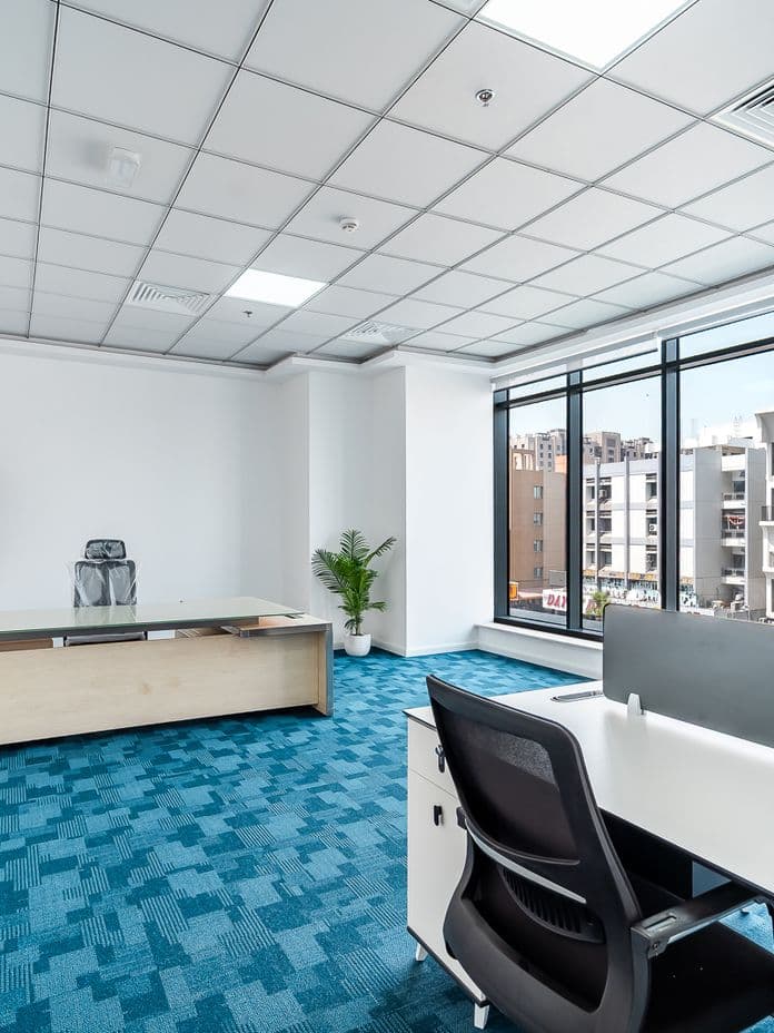 Bright, modern office space in Burj Nahar Building with large windows overlooking a Deira street, blue carpet flooring, and black meeting chairs.