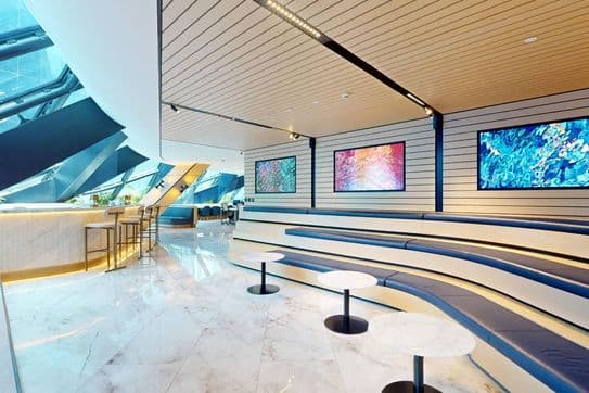 Informal breakout zone with tiered blue leather seating, small marble tables, and vibrant digital art screens on the wall.
