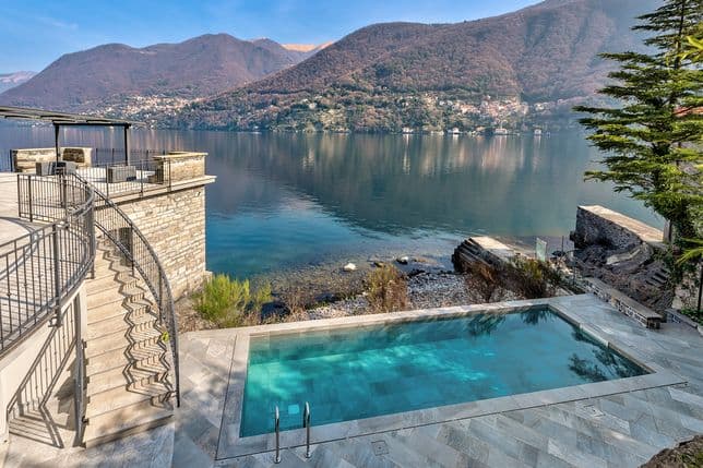 Infinity-Pool mit Blick auf einen ruhigen See mit Bergen im Hintergrund, umgeben von Steinstufen und üppigem Grün.