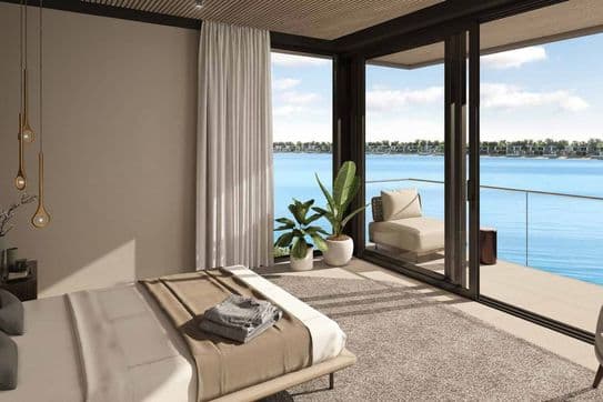 Modern bedroom with large windows overlooking a serene lake. Features a bed, potted plants, and a cozy balcony with seating.