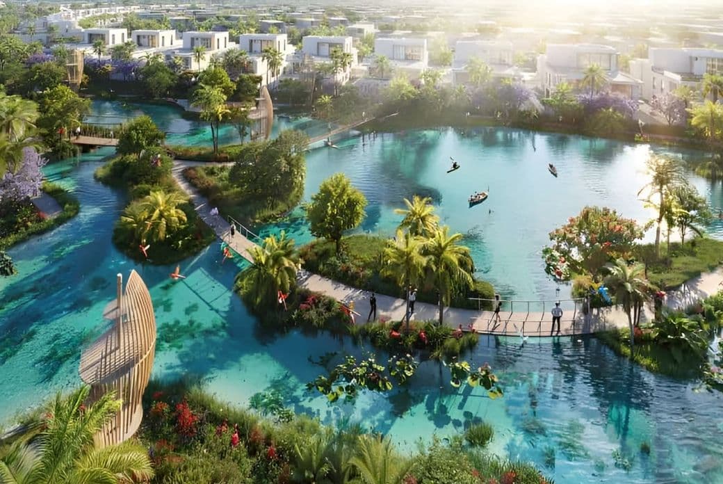 A landscaped lagoon with islands, walking bridges, greenery, kayakers, and modern villas arranged around the water.