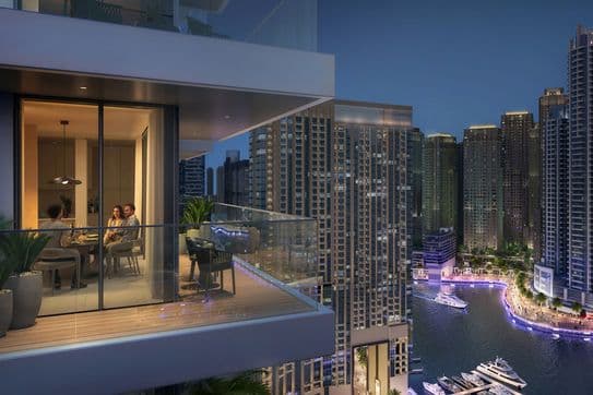 People dining on a balcony overlooking a cityscape and marina at night, with illuminated skyscrapers and boats in the background.