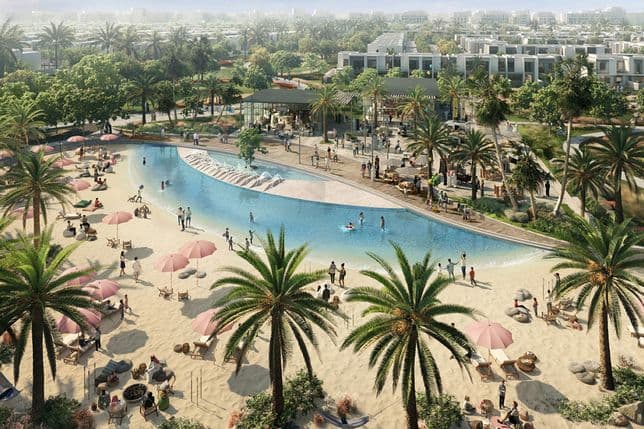 A lively man-made beach in The Valley with people relaxing under pink umbrellas, children playing in the water, and palm trees lining the sandy shore with retail pavilions in the background.