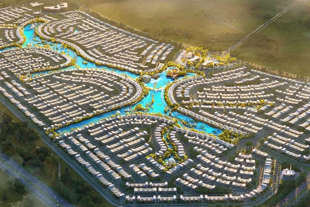 A wide aerial view of a master planned residential community featuring multiple clusters of homes connected by turquoise water channels and green corridors.