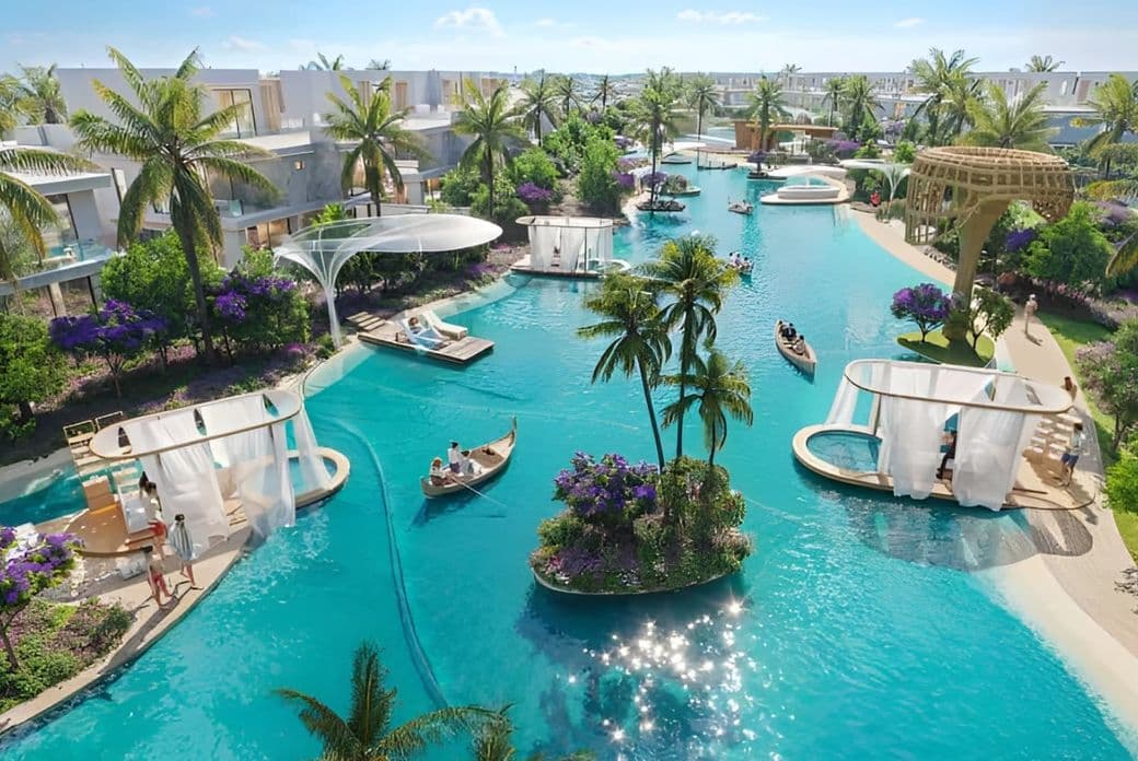 A landscaped residential community featuring a clear blue lagoon with people kayaking, surrounded by greenery, walking paths, tropical plants, and modern villas on both sides.