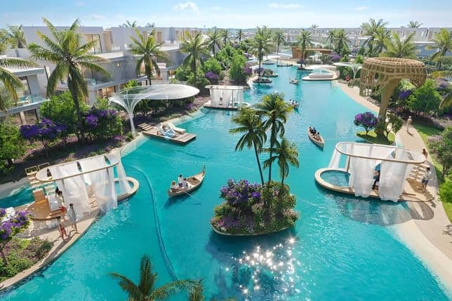 A landscaped residential community featuring a clear blue lagoon with people kayaking, surrounded by greenery, walking paths, tropical plants, and modern villas on both sides.