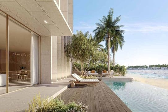 Modern beachfront villa with a wooden deck, lounge chairs, infinity pool, and palm trees under a clear blue sky.