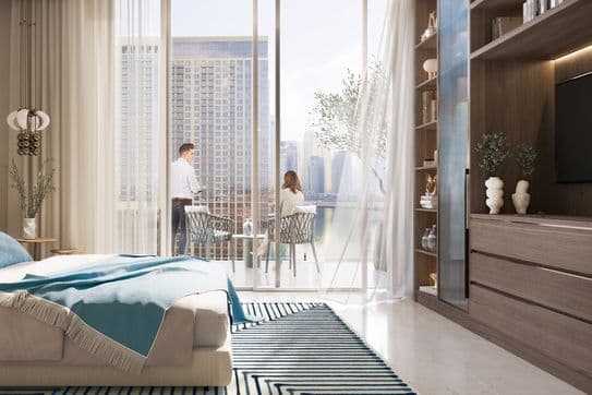Modern bedroom with a large window view of a cityscape. A couple sits at a table on the balcony. Cozy decor with a striped rug and wooden shelves.