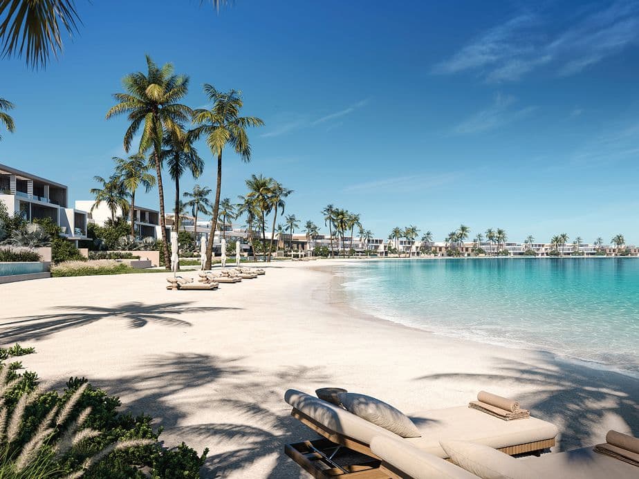 Strandgrundstück mit weißem Sand, türkisfarbenem Wasser und Palmen. Liegestühle stehen am Strand.