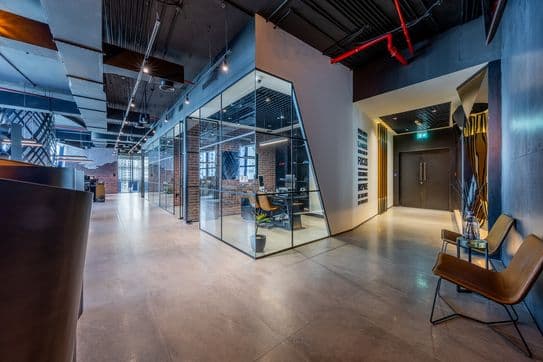Open-plan workspace with exposed ceilings, glass-partitioned meeting rooms, brick accents, and modern lighting fixtures.