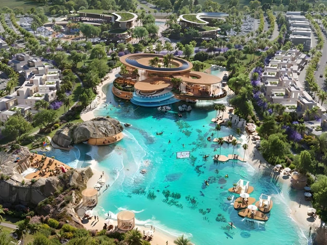 An aerial view of a large lagoon with beaches, rock formations, floating platforms, and a modern clubhouse surrounded by landscaped residential areas.