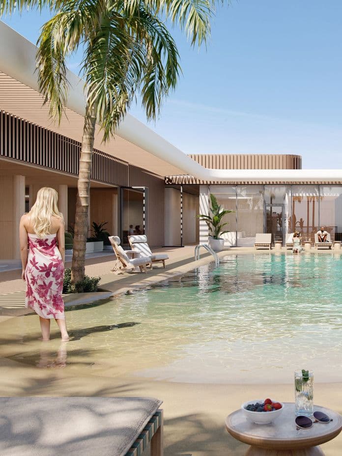 A woman in a floral dress walks by a luxurious pool surrounded by modern architecture, palm trees, and lounge chairs under a clear blue sky.