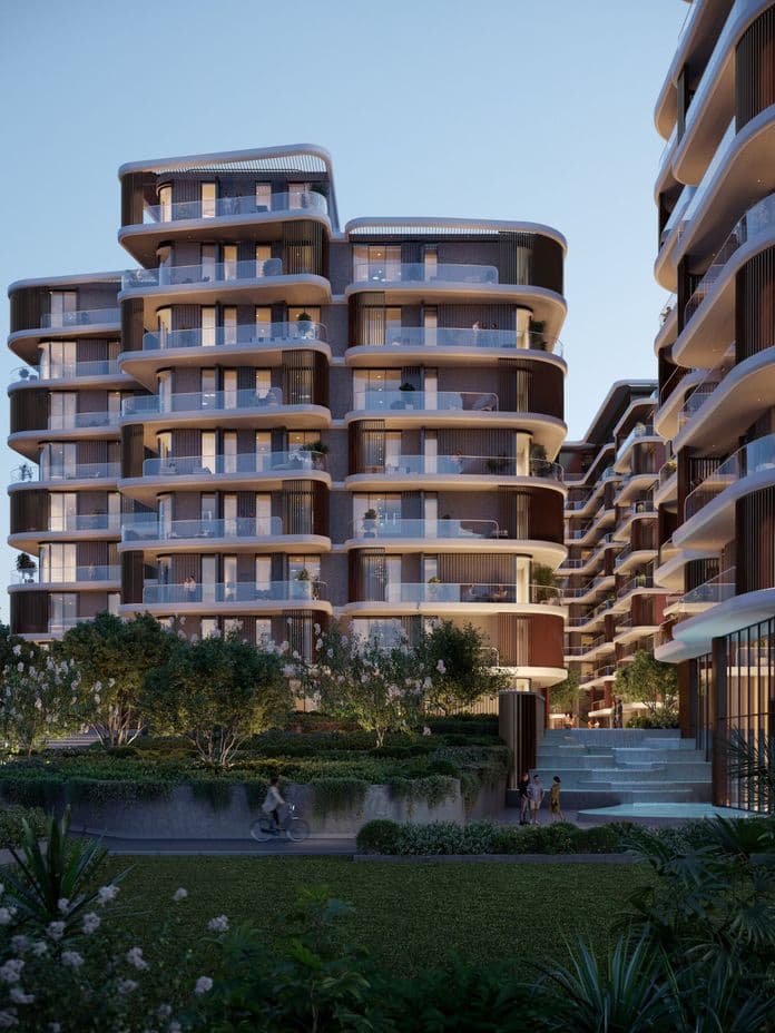 Moderne mehrstöckige Apartmentgebäude mit geschwungenen Balkonen, umgeben von üppigem Grün und einem Fußweg, unter einem klaren blauen Himmel.