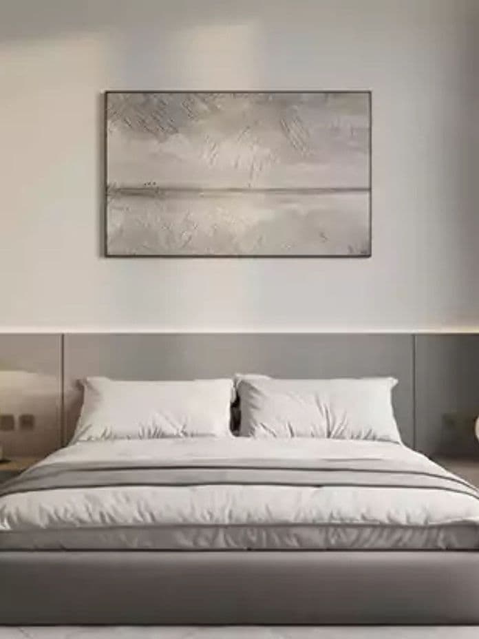 Minimalistisches Schlafzimmer mit neutraler Bettwäsche, grauem Kopfteil und abstrakter Wandkunst.