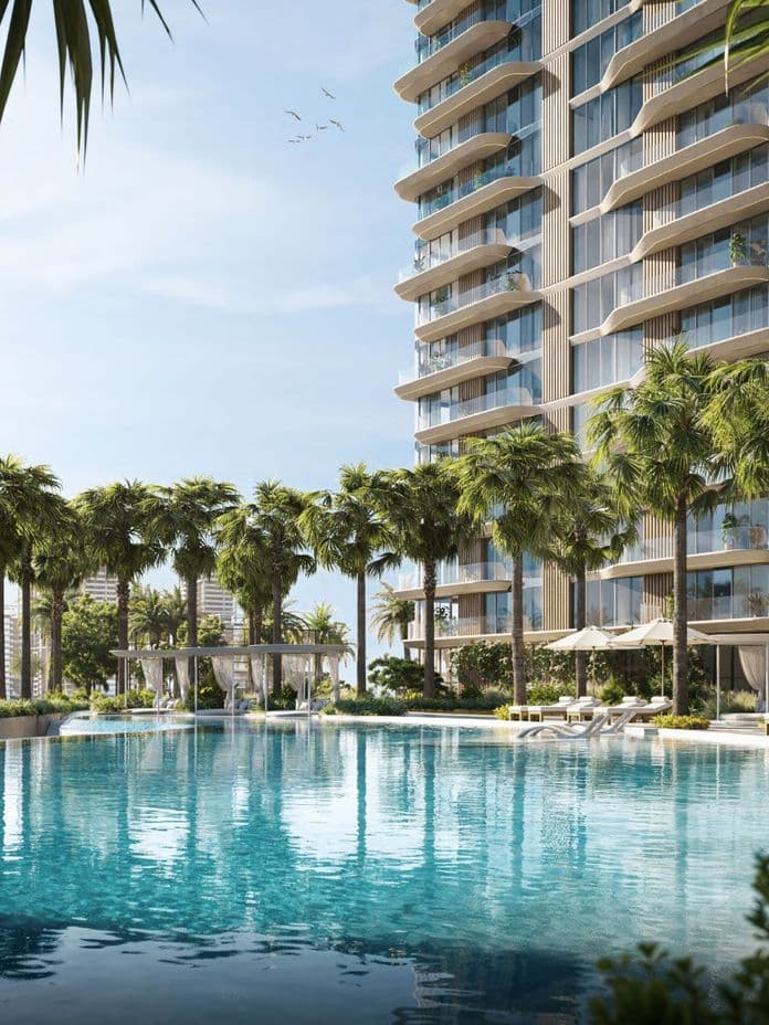 Luxuriöses Hochhaus mit modernem Design, umgeben von Palmen, mit Blick auf einen großen, ruhigen Swimmingpool unter klarem blauem Himmel.