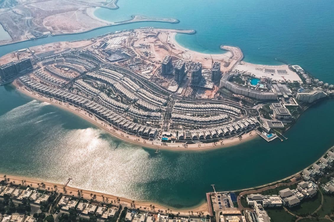 Aerial view of a coastal development with residential housing, surrounded by water and adjacent to a beach and ocean.