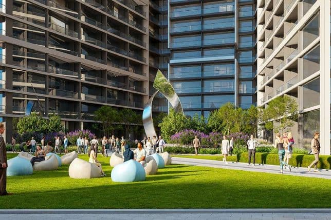 People socialize in a modern outdoor area with grass, trees, and bean bag seating, surrounded by tall glass buildings under a clear sky.