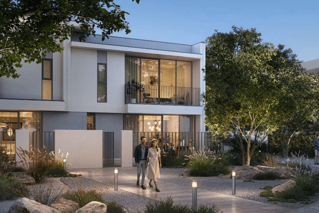 A contemporary townhouse at Vindera at The Valley with landscaped pathways, evening lighting, greenery, and residents walking through the community.