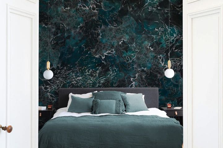 Vue d'une chambre à coucher à travers des portes blanches ouvertes. Un lit vert avec des coussins est placé contre un mur sombre à motif de marbre avec des lumières suspendues.