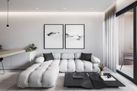 Bright living room with a white tufted sectional, black-framed mountain prints, a low black coffee table, and glass doors with sheer curtains.